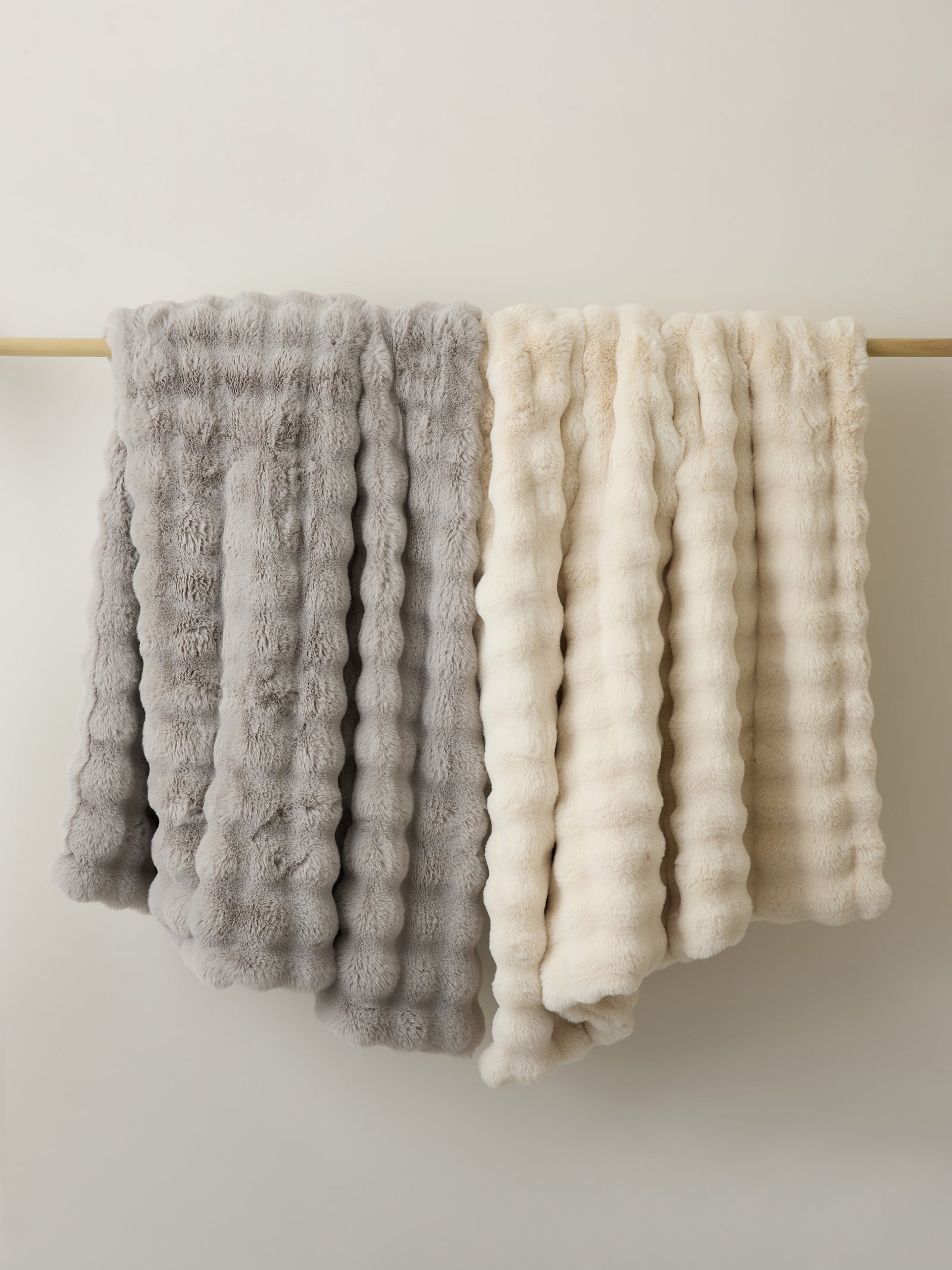 Light grey and creme lush faux fur blankets hanging on wooden rail