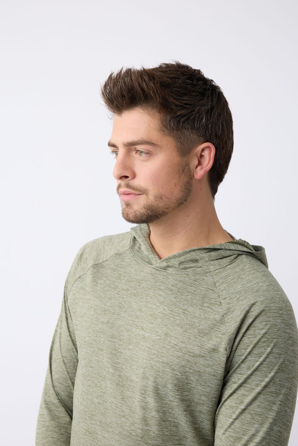 A person with short dark hair and facial hair is wearing a Cozy Earth's Men's Lightweight Performance Hoodie in light green. They are looking to the left against a plain white background. 