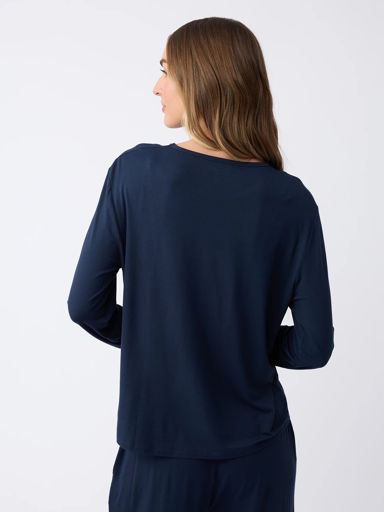 A person with long brown hair stands with their back to the camera, wearing a Cozy Earth Women's Stretch Knit Bamboo Long Sleeve Lounge Tee against a plain white background. |Color:Navy