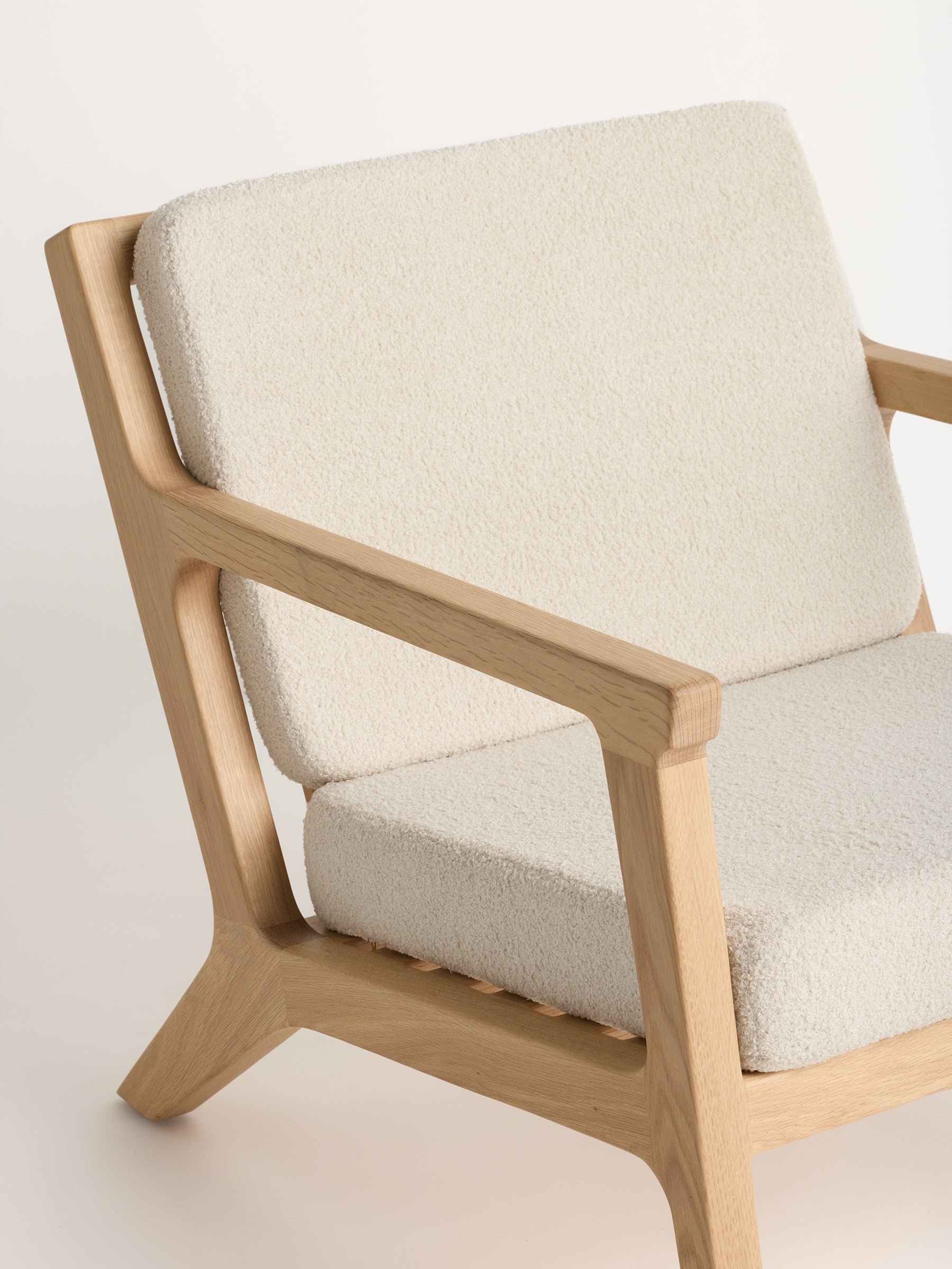 Introducing the Coronado Lounge Chair by Cozy Earth: a modern armchair with a light wood frame and cream-colored, textured cushions. It boasts simple, clean lines and a minimalist design, emphasizing both comfort and elegance. 