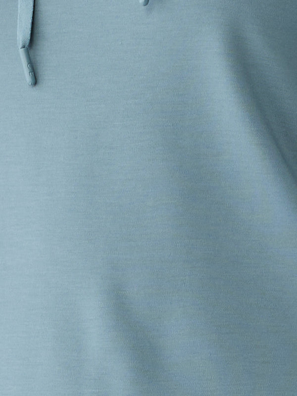 Close-up of a light blue fabric from the Women's Ultra-Soft Bamboo Hoodie by Cozy Earth, showcasing a slightly textured surface with a seam and drawstrings on the upper left side. The fabric appears soft and smooth, likely indicating its high-quality bamboo material. 