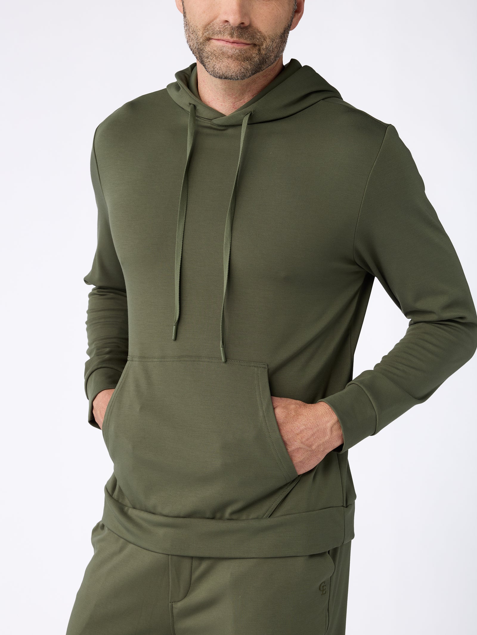 A man wearing a Cozy Earth Men's Ultra-Soft Bamboo Hoodie with his hands in the front pocket, standing against a plain background. 