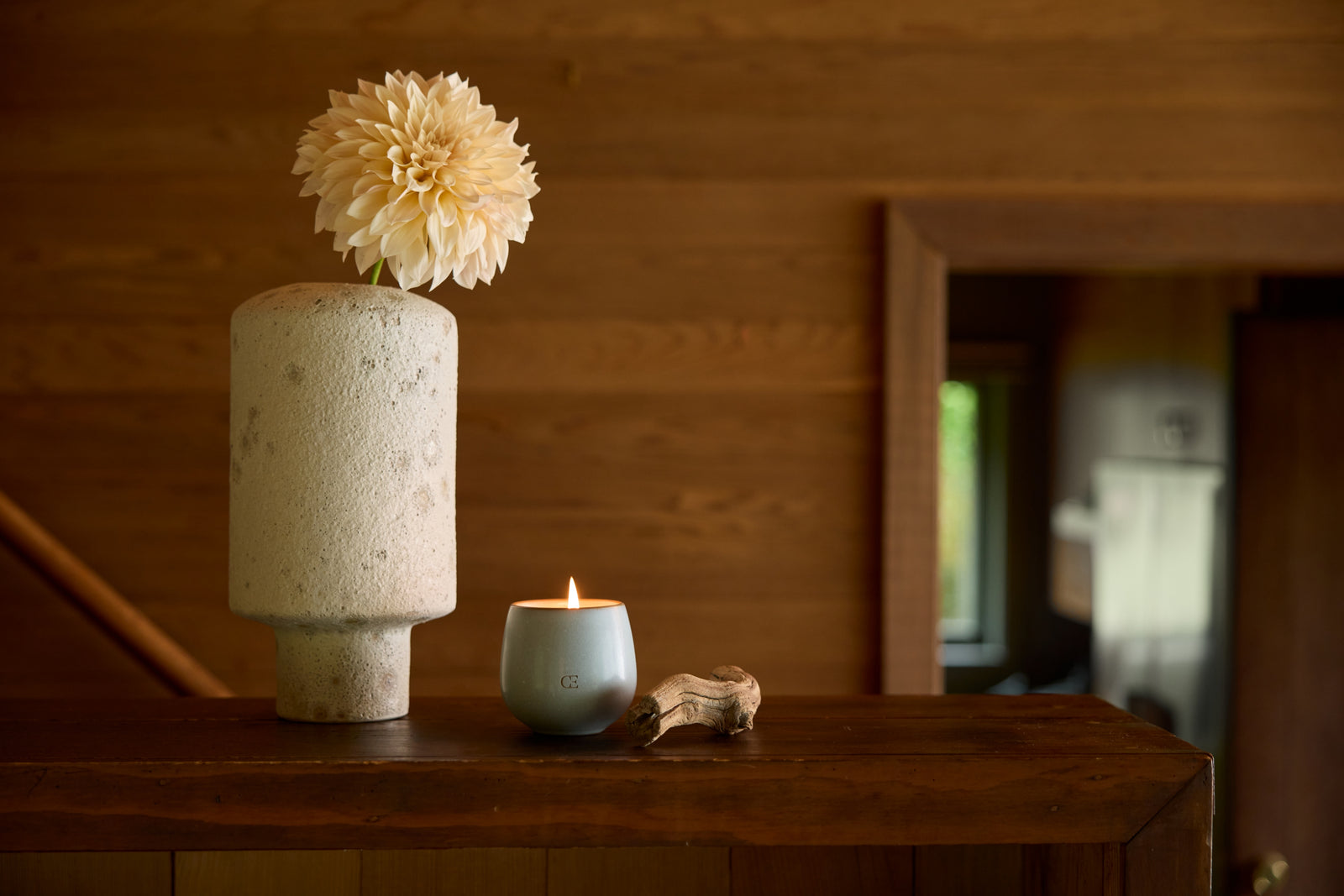 Cozy Earth Gather Candle sits on a shelf near a vase and driftwood