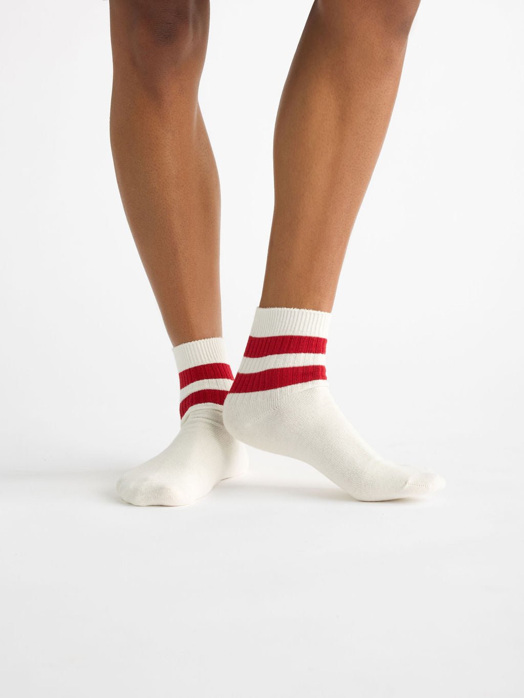 Two legs wearing Cozy Earth's Women's Sadie Socks, white with red stripes at the top, crossed on a plain white background. 