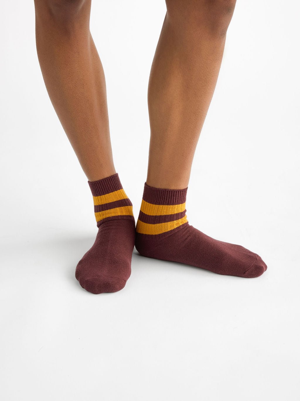 A person wearing Cozy Earth's Women's Sadie Sock in burgundy with two yellow ankle stripes, standing against a plain white background. 