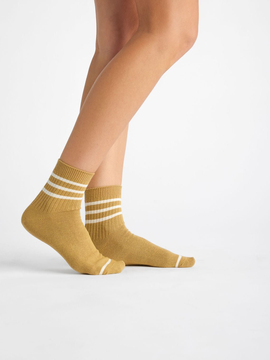 A person wearing Cozy Earth's Women's Sadie Sock in mustard-yellow with white stripes stands on a white background. 