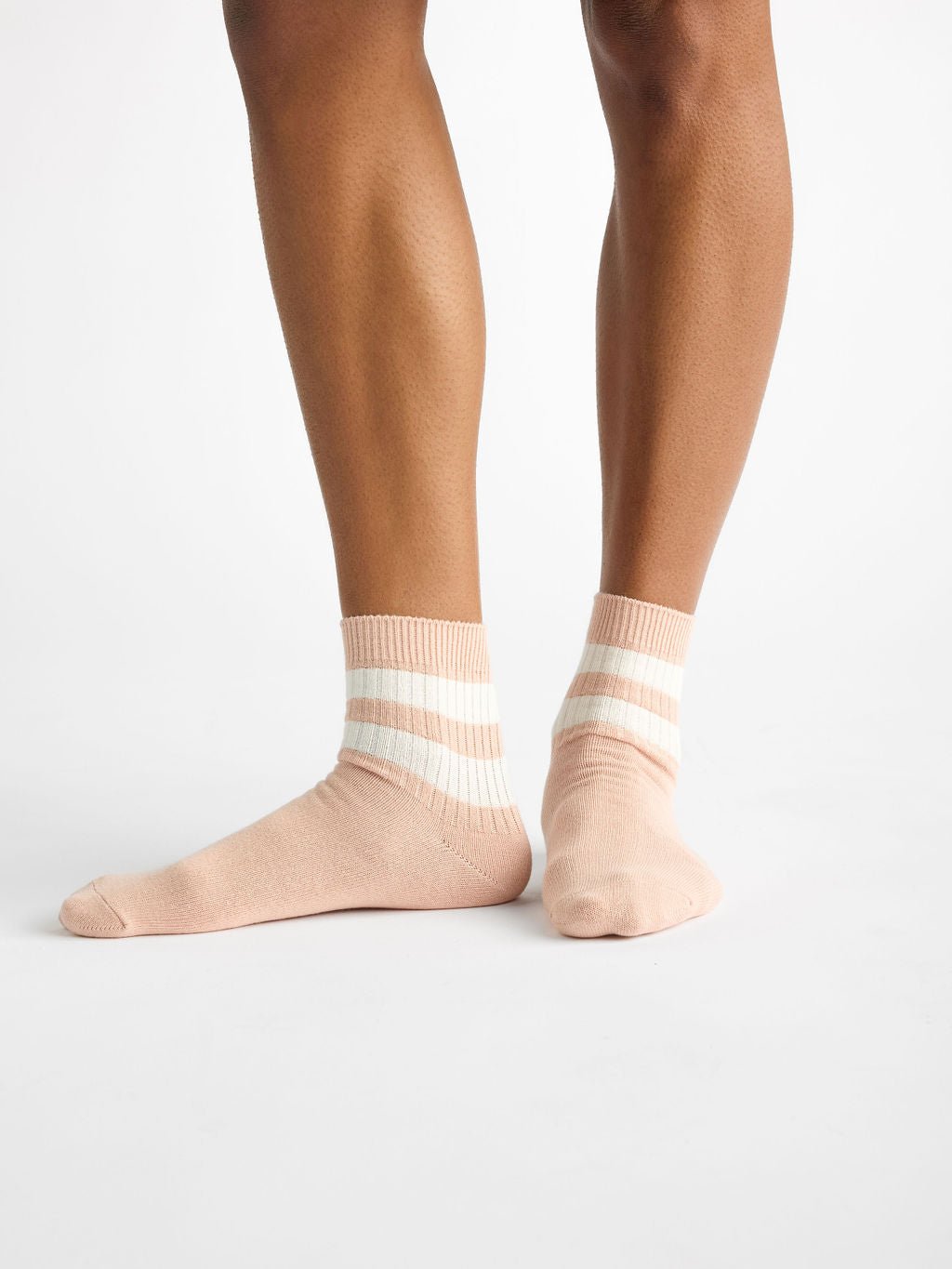 A person is standing on a plain white background wearing the Women's Sadie Sock by Cozy Earth in light beige, featuring two white stripes. 