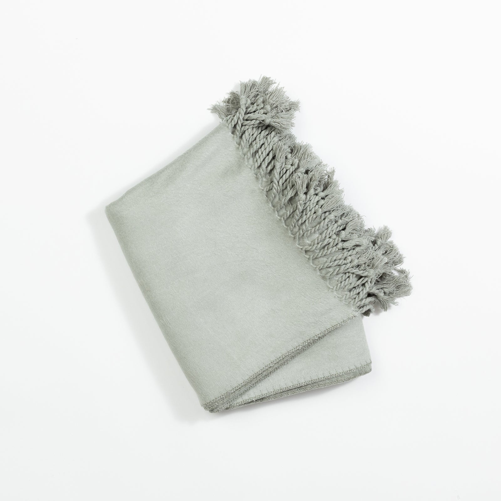 The Bamboo Tassel Throw by Cozy Earth, neatly folded in light gray with decorative tassels along one edge, is displayed on a plain white background. The tassels add a textured contrasting detail to the smooth fabric of the blanket. 