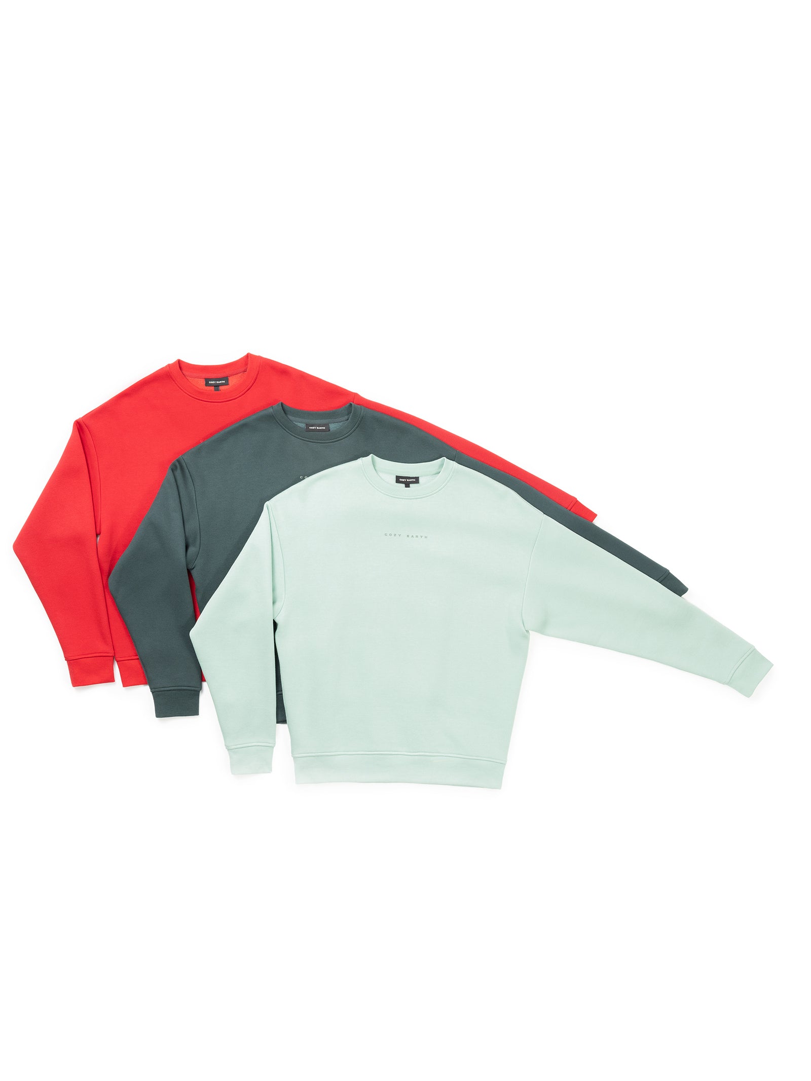 Three Women's CityScape Crewneck sweatshirts from Cozy Earth are arranged in a layered display. The sweatshirts are mint green at the front, followed by dark green in the middle, and red at the back, each featuring a simple design with minimal branding. 