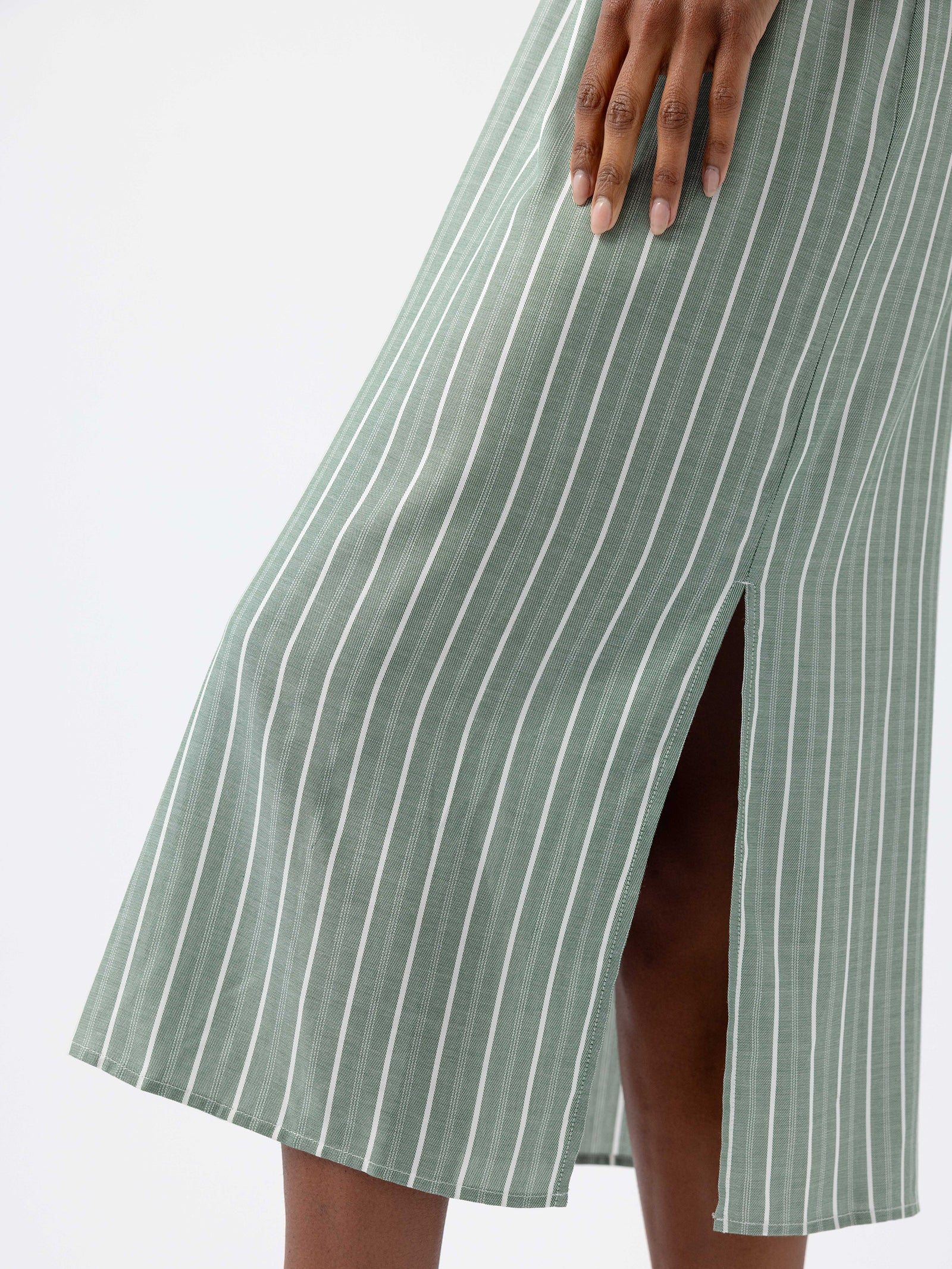 A person is seen wearing the Cozy Earth Women's Soft Woven Nightgown, featuring a green striped pattern with a front slit, against a plain white background. Their hand gently touches the fabric, highlighting its texture and vertical stripes. 