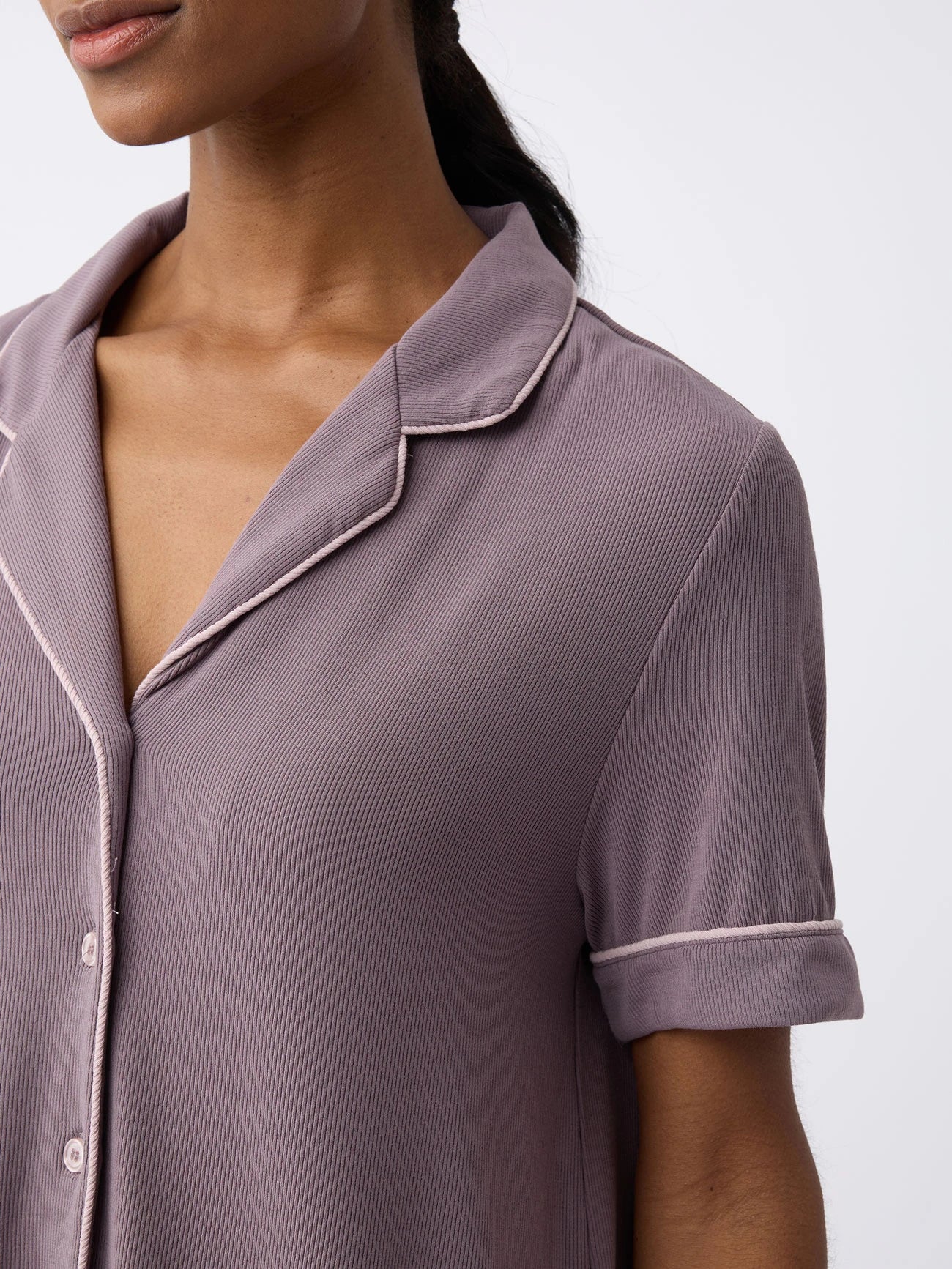 The focus is on the upper part of a Twilight Women's Bamboo Rib-Knit Classic Short Sleeve Pajama Top by Cozy Earth, showcasing its notched collar, button details, and lilac piping. |Color:Twilight