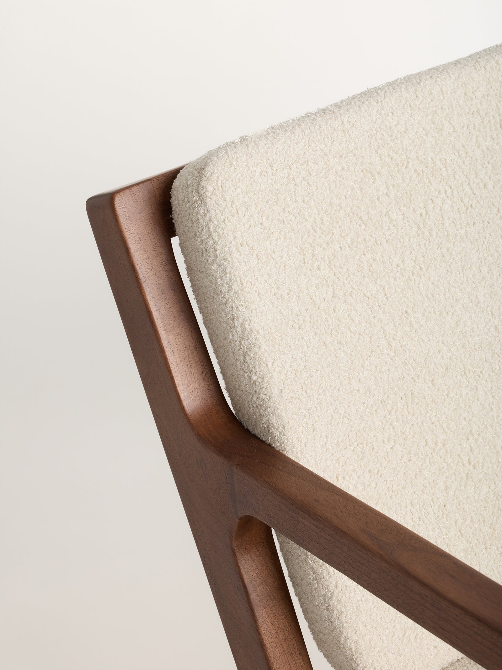 Close-up of the Coronado Lounge Chair by Cozy Earth, showcasing a wooden frame and a textured, cream-colored fabric cushion. The image highlights the chair's minimalist design and material contrast. 