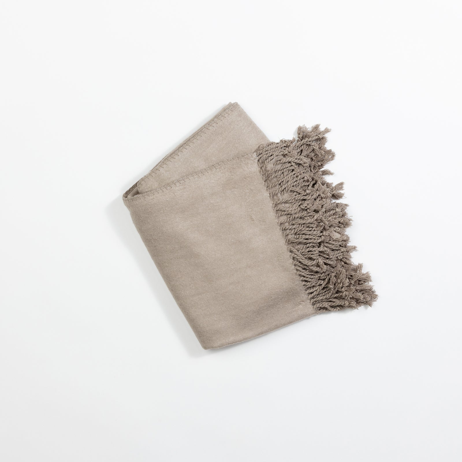 A neatly folded Bamboo Tassel Throw by Cozy Earth in light beige, featuring fringed tassels along one edge, placed on a white background. 