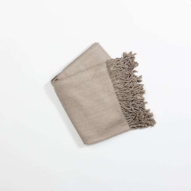 A neatly folded Bamboo Tassel Throw by Cozy Earth in light beige, featuring fringed tassels along one edge, placed on a white background.