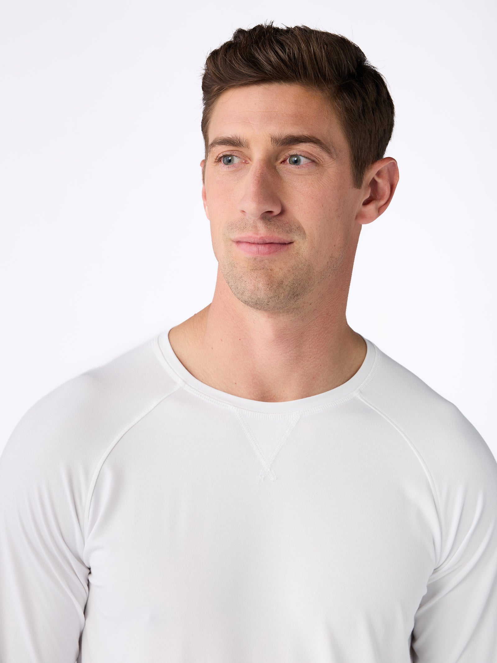 A man with short brown hair is wearing a white Men's Stretch-Knit Bamboo Long Sleeve by Cozy Earth. He is looking off to the side, with a neutral expression against a plain white background. 