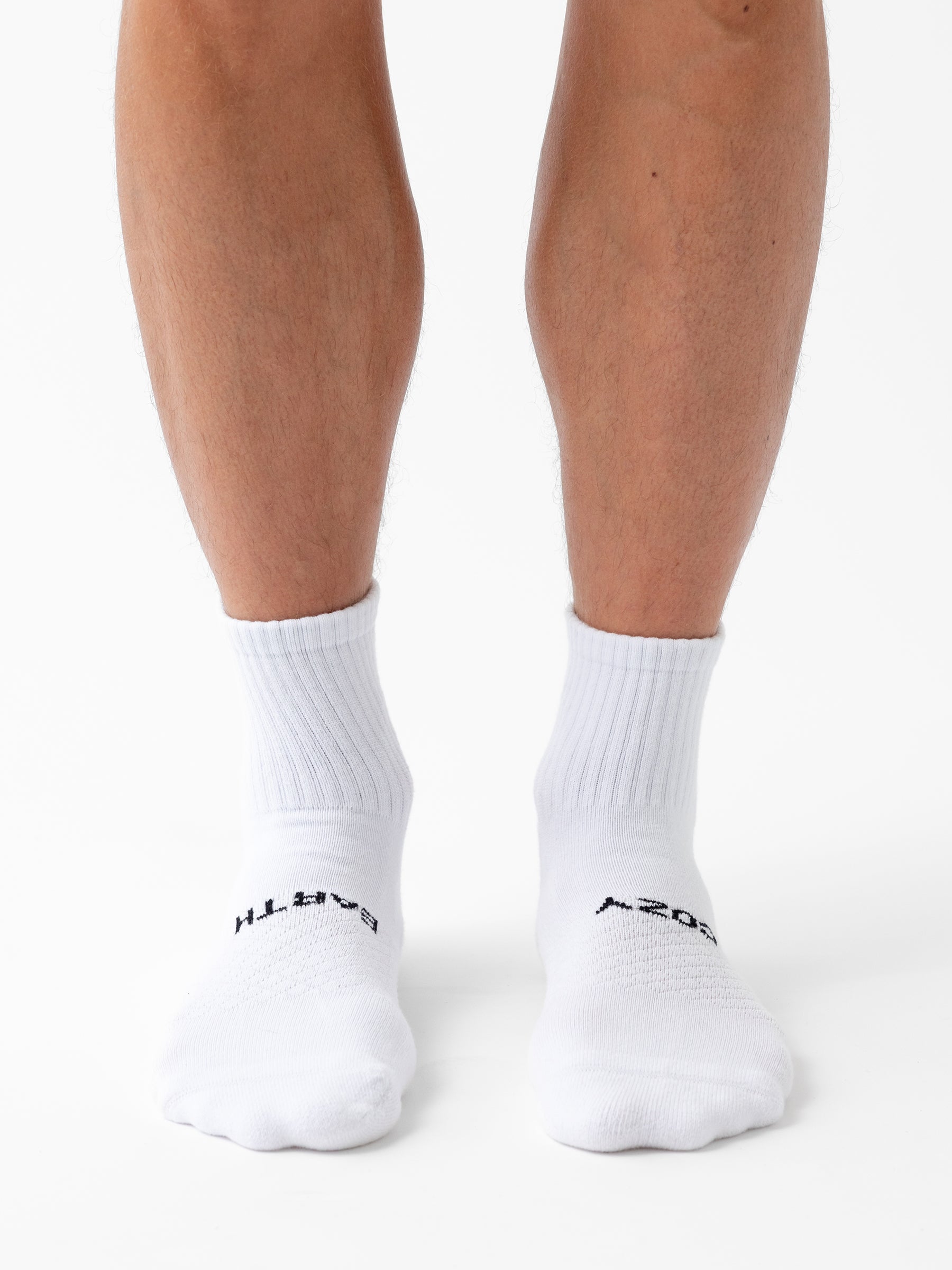 A person wearing Cozy Earth's Essential Quarter Sock 6-Pack stands on a white surface, showing only their lower legs and feet. 