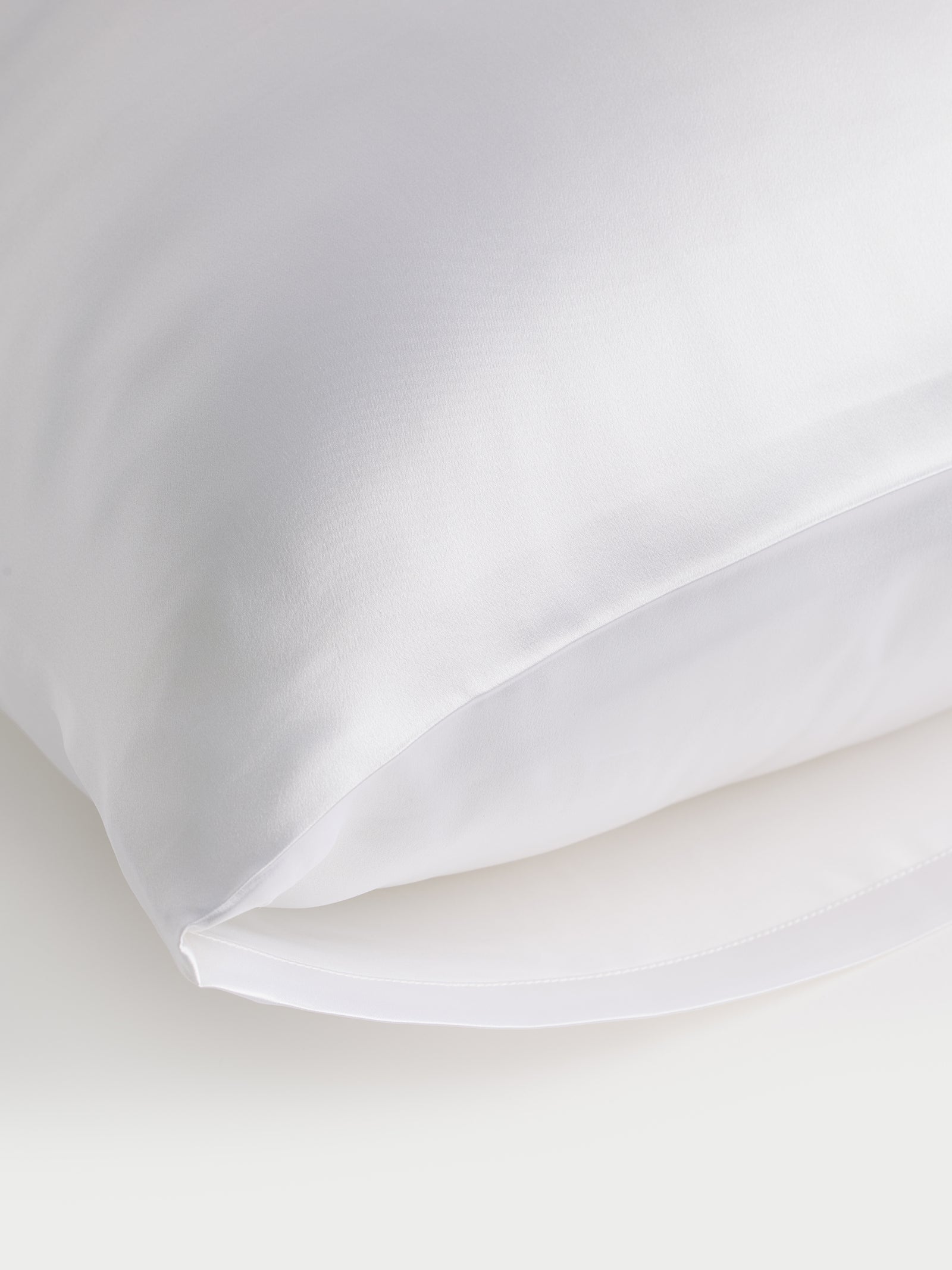 A close-up of a Cozy Earth Silk Pillowcase with a sleek, pristine surface is visible. The pillowcase partially stands out against a white background, showcasing its silky texture and inviting allure. 