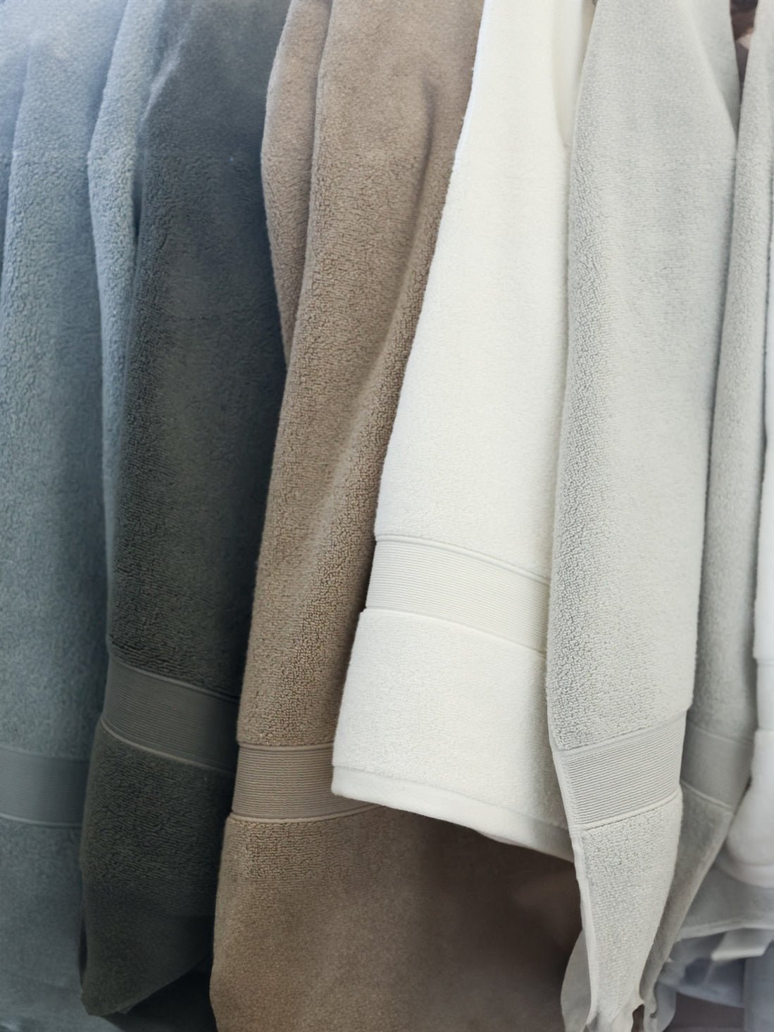White, sand, light grey, harbor mist, charcoal, and seashell luxe bath towels hanging side by side 