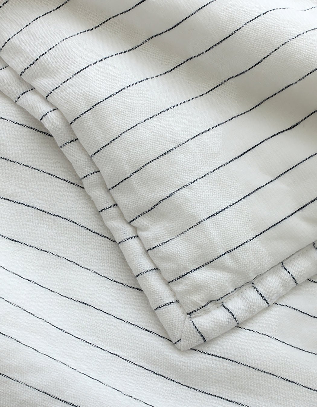 A close-up of Cozy Earth's Linen Pencil Stripe Quilted Shams, featuring white fabric with thin, evenly spaced black stripes, overlapping layers, and a soft, smooth texture.