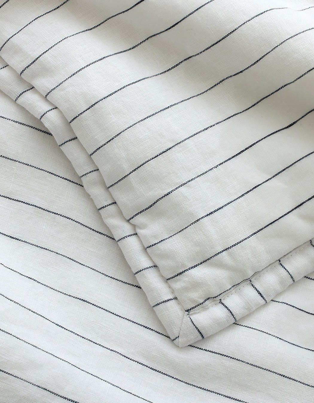 A close-up of Cozy Earth's Linen Pencil Stripe Quilted Shams, featuring white fabric with thin, evenly spaced black stripes, overlapping layers, and a soft, smooth texture.