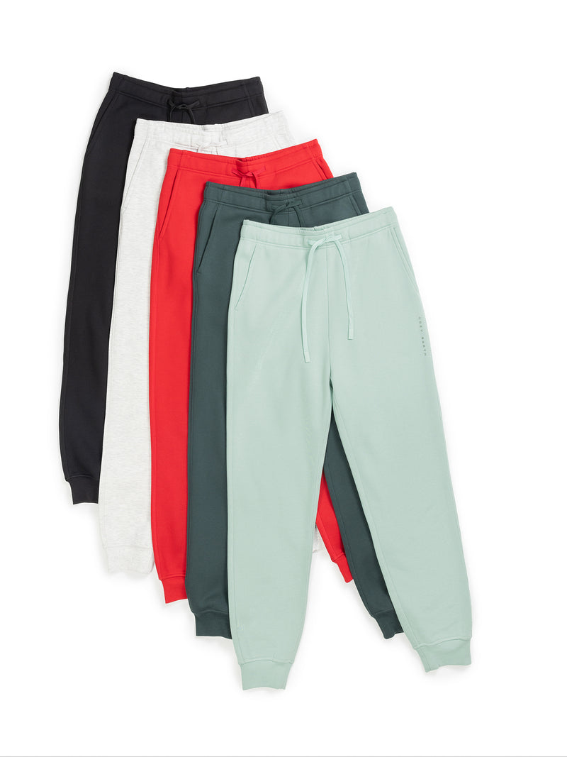 Five pairs of Men's CityScape Joggers by Cozy Earth in black, white, red, teal, and mint green are neatly stacked to display their color variety. Each jogger features drawstrings and elastic cuffs, arranged against a white backdrop.