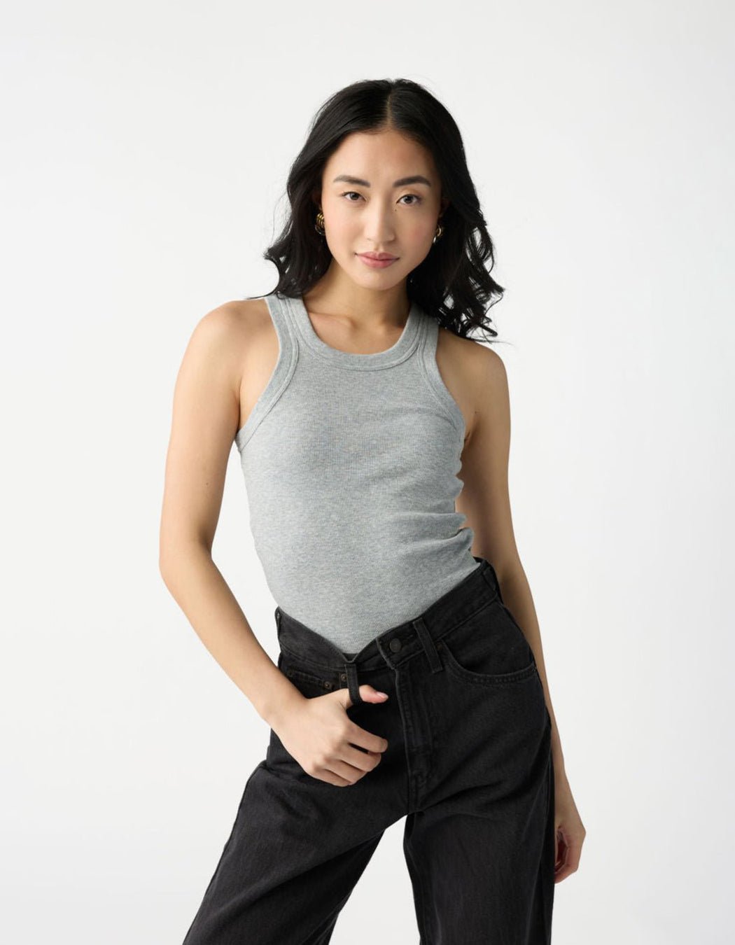 A woman with long black hair poses confidently in a Cozy Earth Women's Fine Ribbed Tank, paired with black jeans, against a plain white background. |Color:Heather Grey