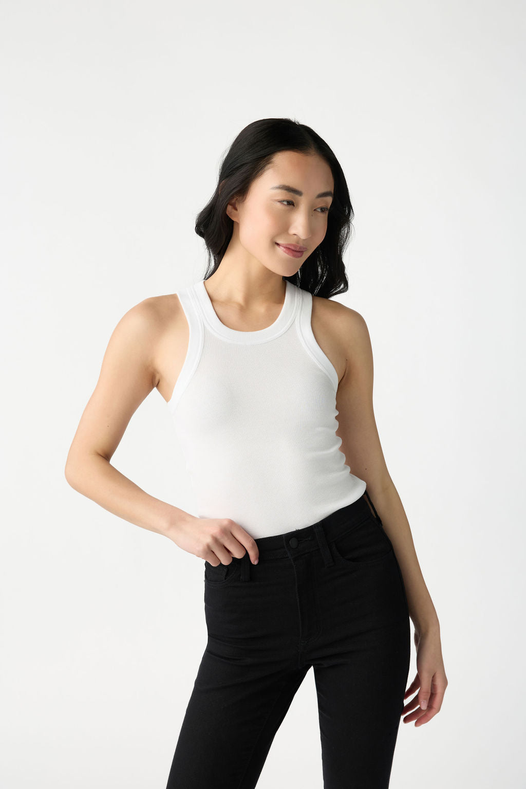 A dark haired woman wears Cozy Earth Women's Fine Ribbed Tank in White. She wears black jeans and stands in front of a white background. 