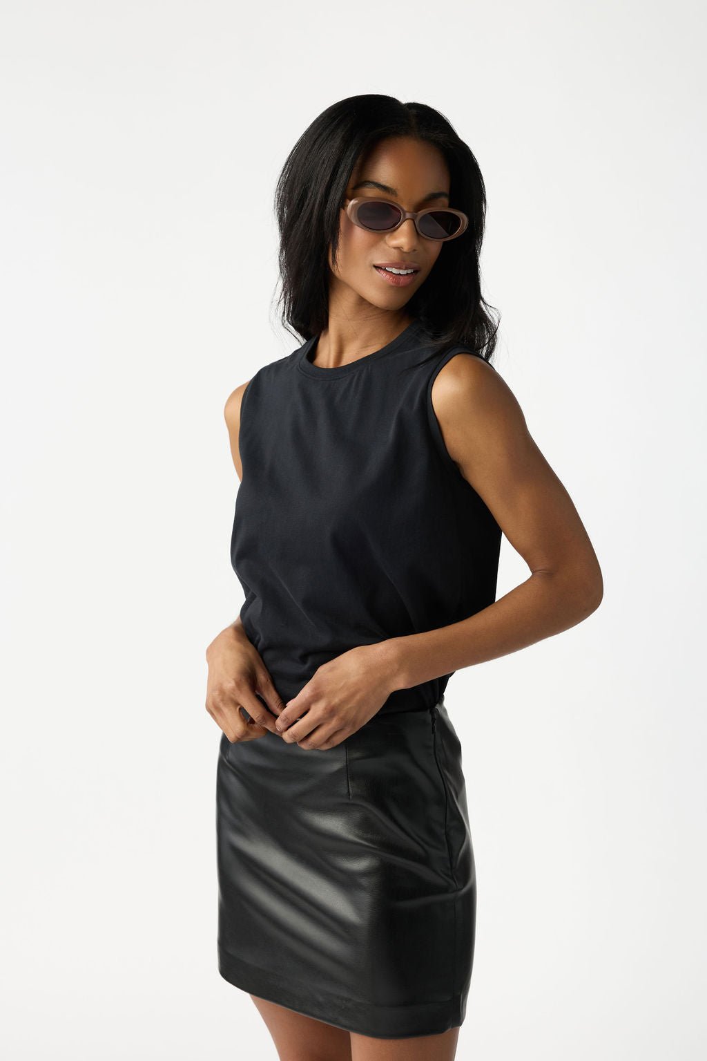 A smiling woman with dark hair wearing sunglasses has on the Cozy Earth Women's All Day Sleeveless Tee in Jet Black. She's shown from the thighs up in front of a white background. |Color:Jet Black
