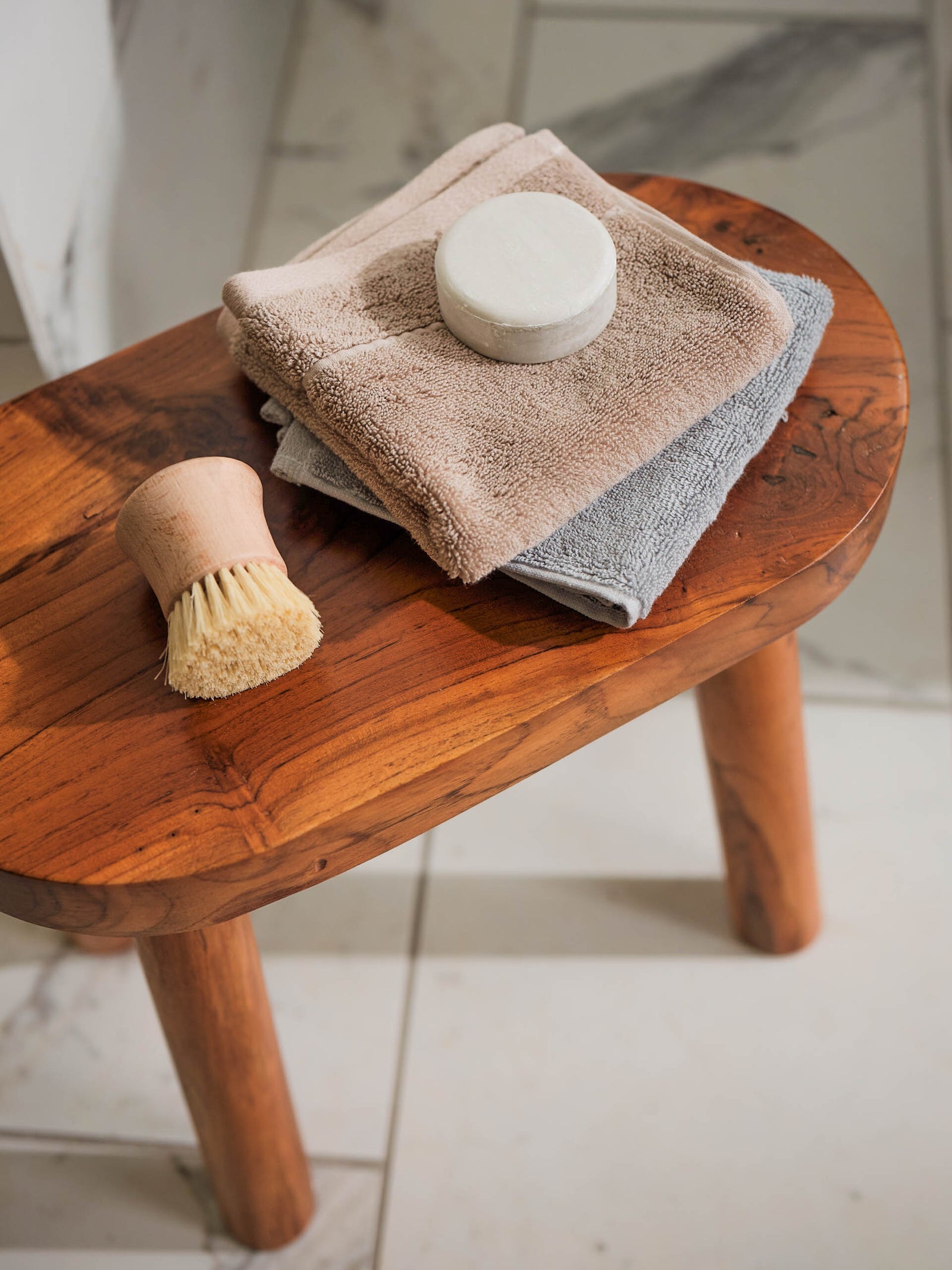 Premium Plush Hand Towels in the color Sand and Harbor Mist. Photo of Sand and Harbor Mist Premium Plush Hand Towels taken resting on a stool in a bathroom with marble tile.
