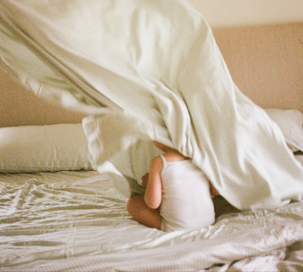 Child lying under a blanket on a bed in a bedroom setting