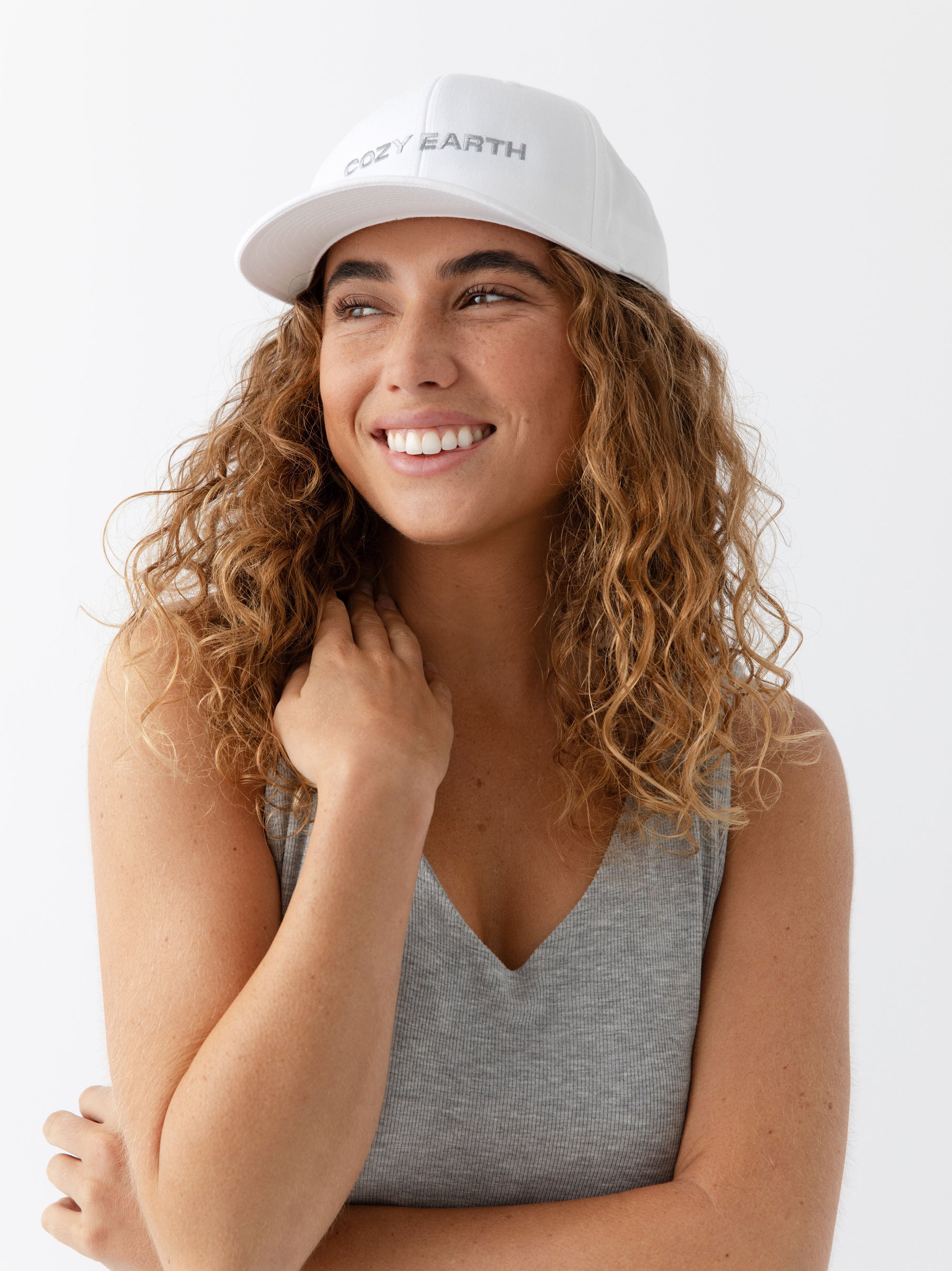 A woman wearing a White cap with 'COZY EARTH' text on a white background 