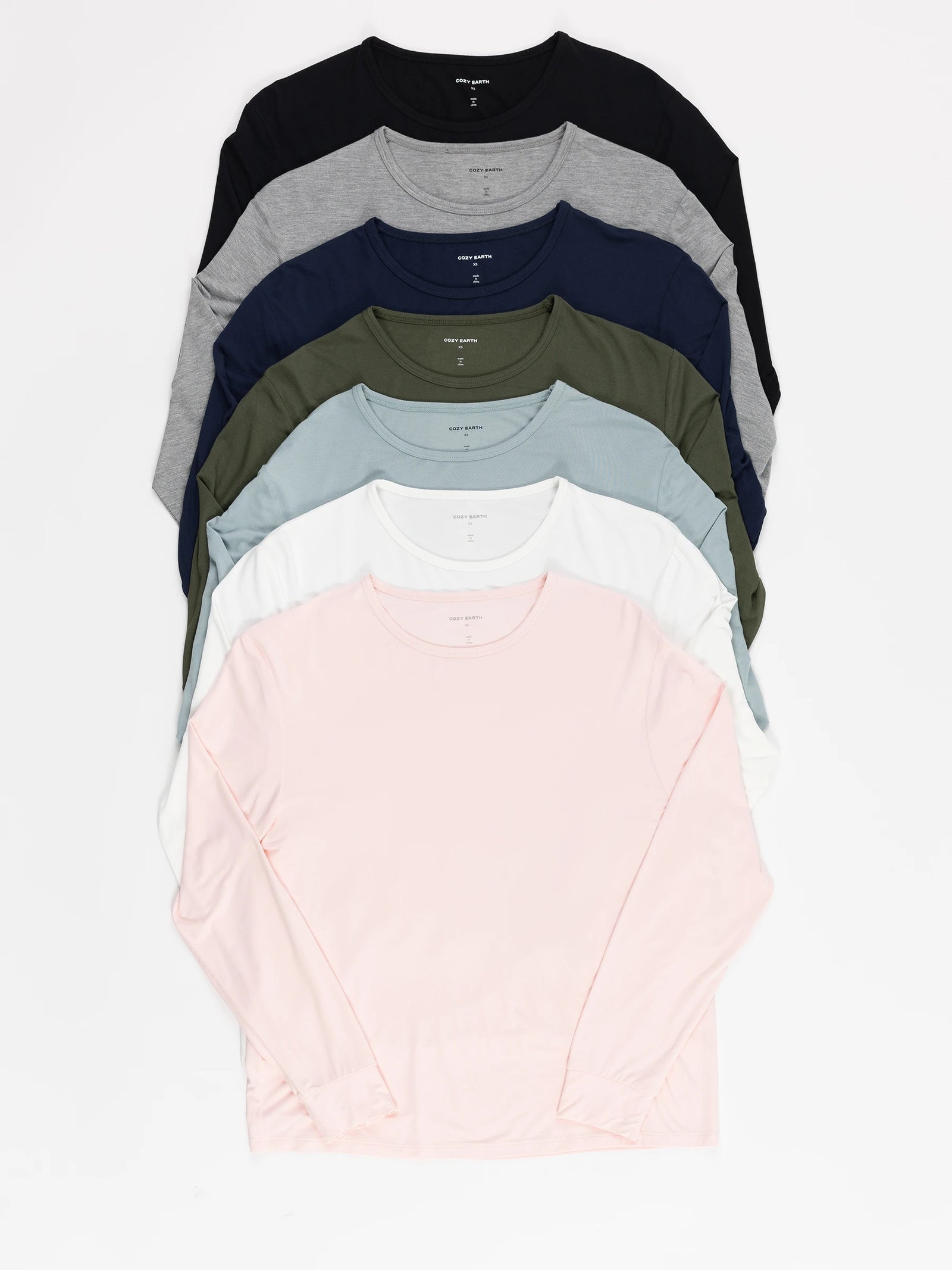 A neatly stacked display of Women's Stretch Knit Bamboo Long Sleeve Lounge Tees by Cozy Earth features identical long-sleeve shirts with round necklines in black, navy, gray, green, light blue, white, and pink. 