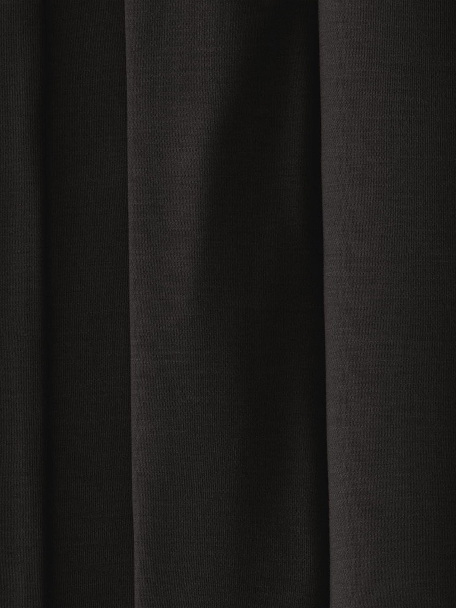 A close-up of the Men's Stretch-Knit Long Sleeve Bamboo Pajama Jogger Set by Cozy Earth, showcasing a dark, solid-colored fabric with soft, vertical folds. The fabric has a smooth texture with minimal visible details, creating a simple and elegant appearance. The lighting gently highlights the contours of the folds. 