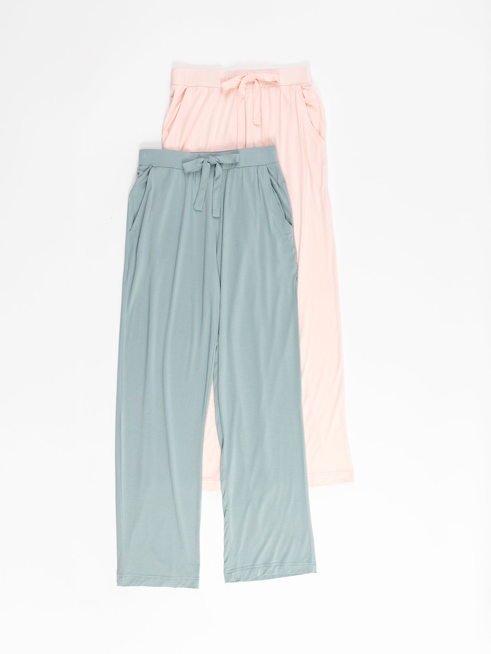 Two pairs of Stretch Knit Bamboo Pants by Cozy Earth on a white background. One pair is light pink, and the other is light blue-green. Both feature drawstring waistbands and relaxed, flowing fabric. 