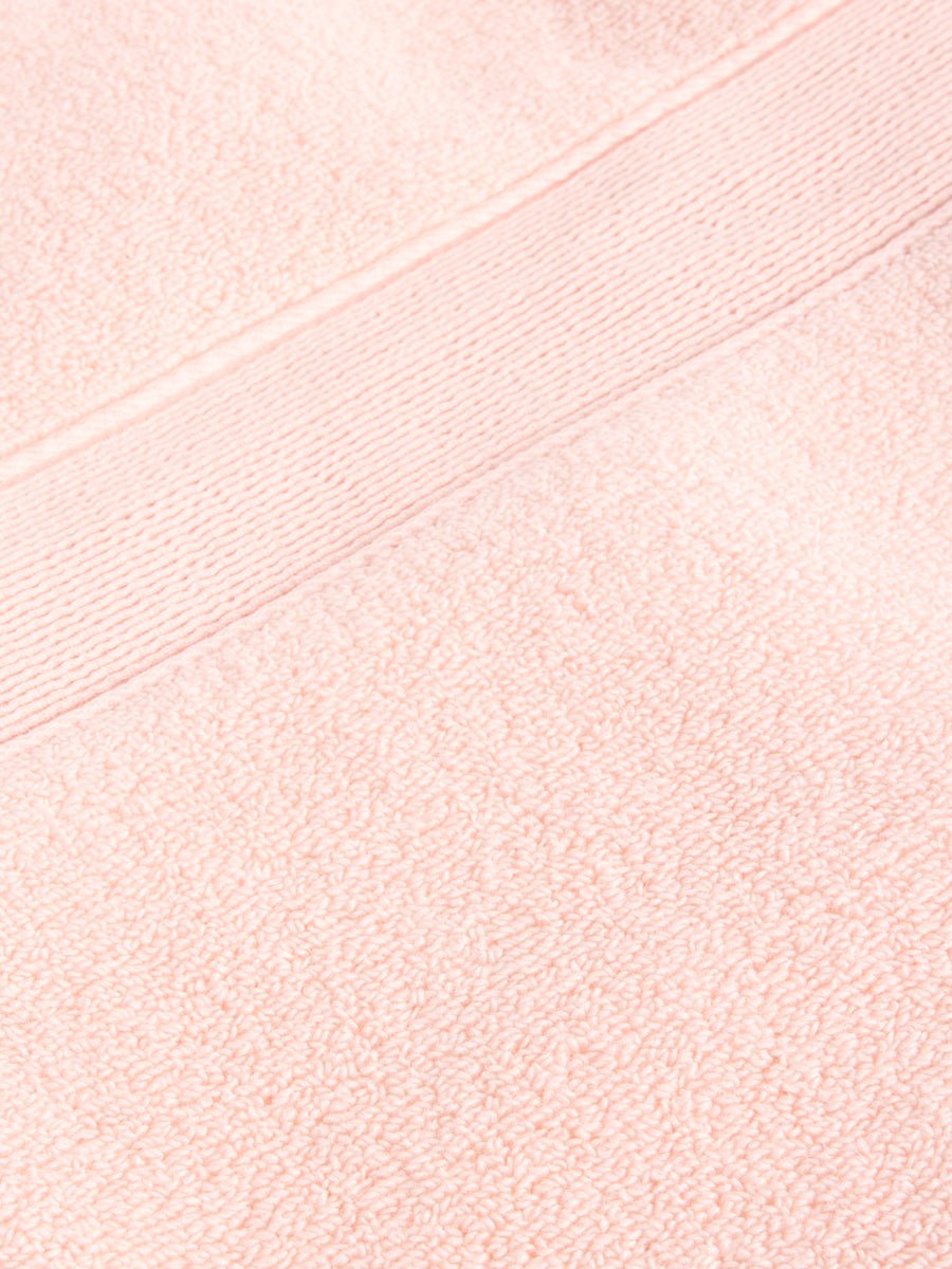 Close-up of Cozy Earth's Luxe Bath Towel Set, featuring a peach-colored, textured weave with a decorative horizontal band. The plush and absorbent fabric is ideal for personal or home use. 