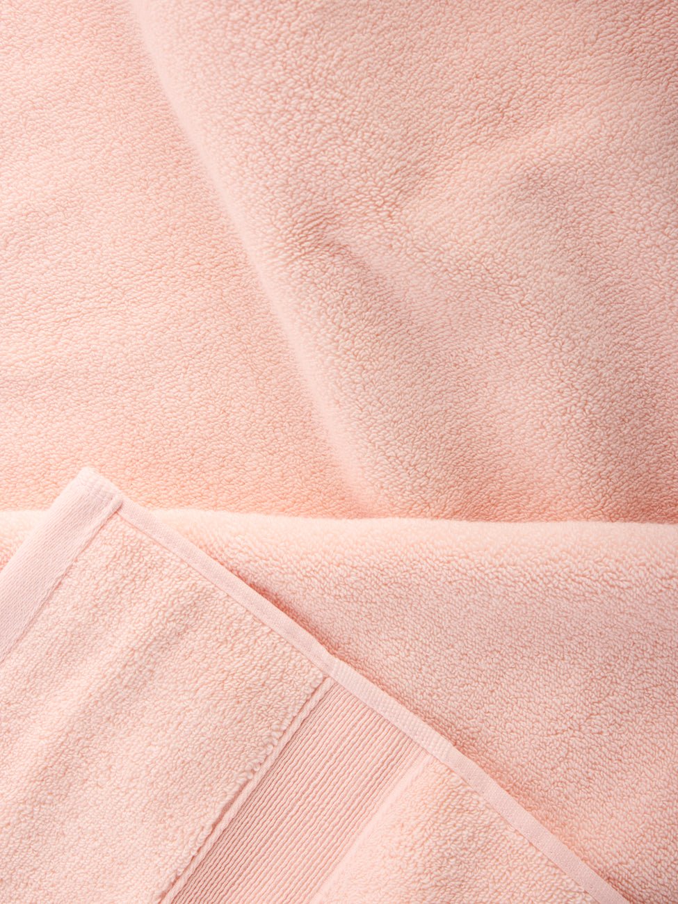 Close-up of Luxe Bath Sheets in a soft, light pink by Cozy Earth. The fabric looks plush and thick with visible texture and stitching at the edges, capturing a sense of coziness and comfort. 