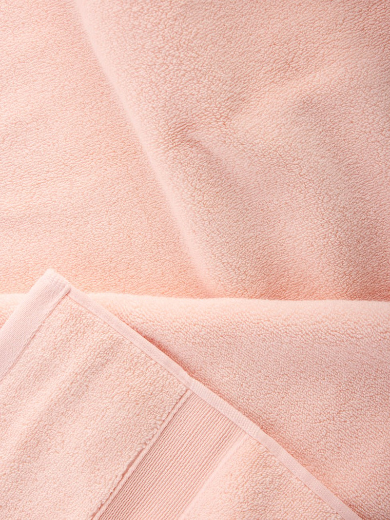 Close-up of Luxe Bath Sheets in a soft, light pink by Cozy Earth. The fabric looks plush and thick with visible texture and stitching at the edges, capturing a sense of coziness and comfort.