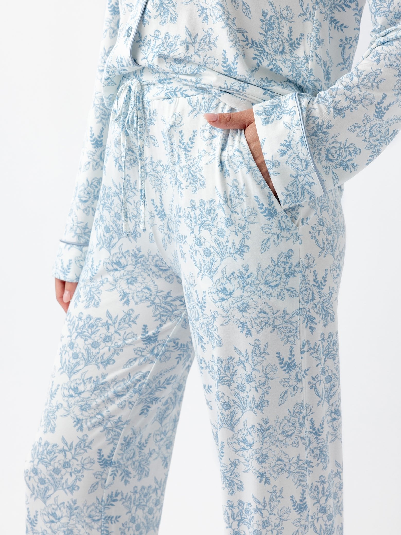 A person is wearing Cozy Earth Women's Bamboo Stretch-Knit Pajama Pant, featuring a blue floral pattern on white, relaxed fit with a drawstring waist. One hand is in the pocket against a neutral background. 