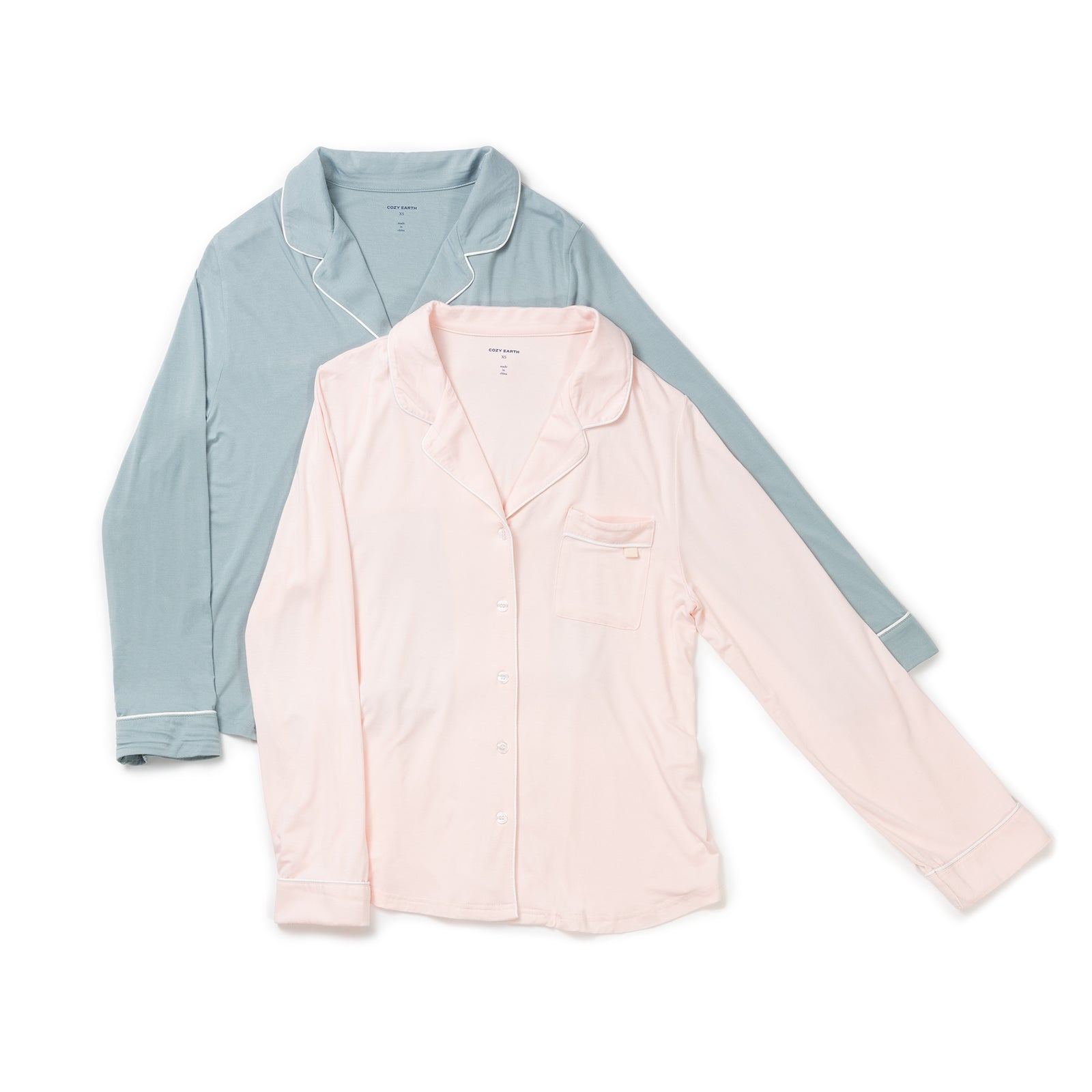 Two Women's Long Sleeve Bamboo Pajama Tops in Stretch-Knit from HIDE are laid out overlapping each other. One is light pink with a breast pocket and buttons down the front, while the other is light blue with white piping and also features a front pocket and buttons. Both have collars. 