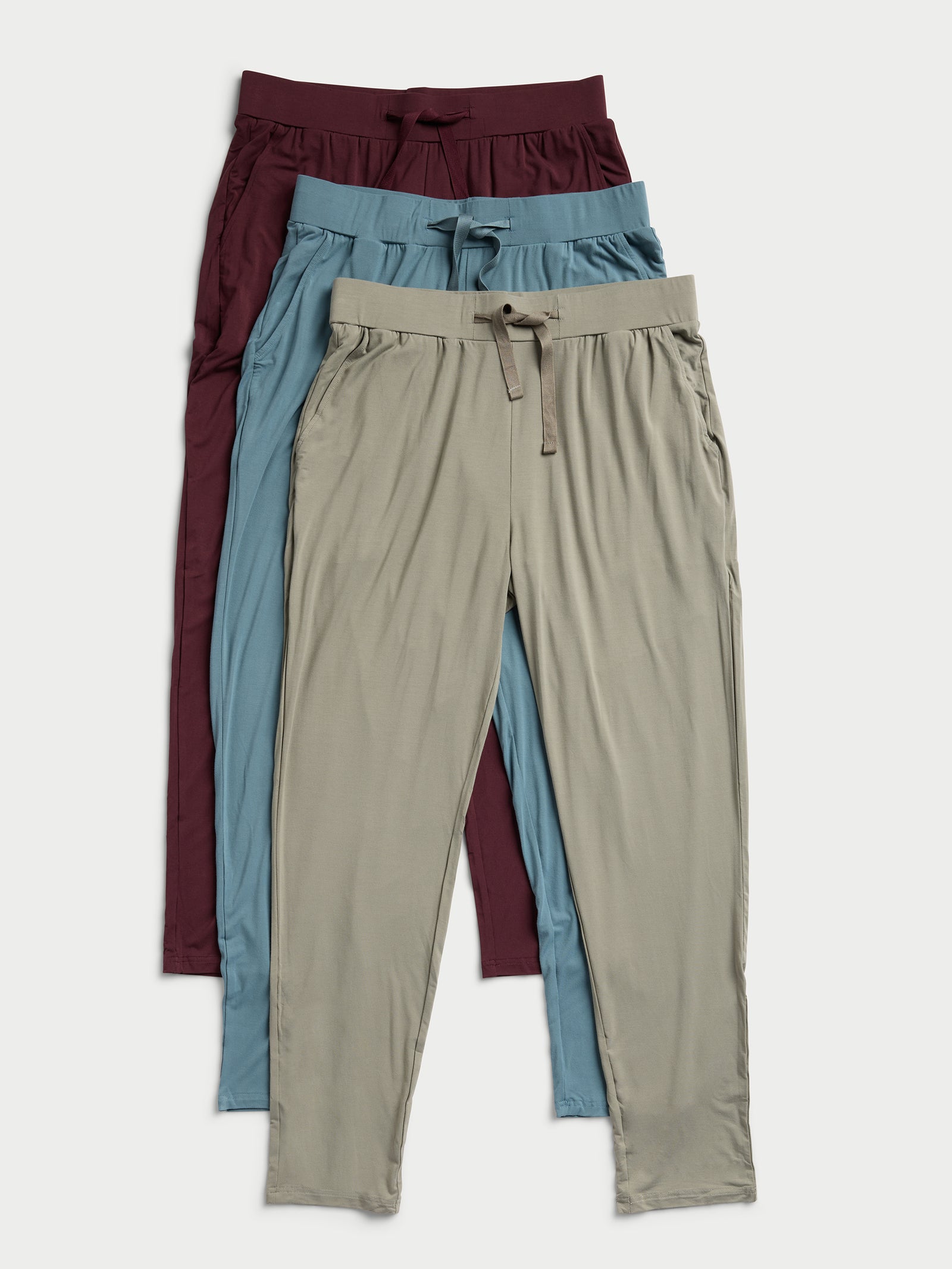 A set of three Cozy Earth Men's Stretch-Knit Bamboo Pajama Pants in burgundy, blue, and beige are neatly stacked. 