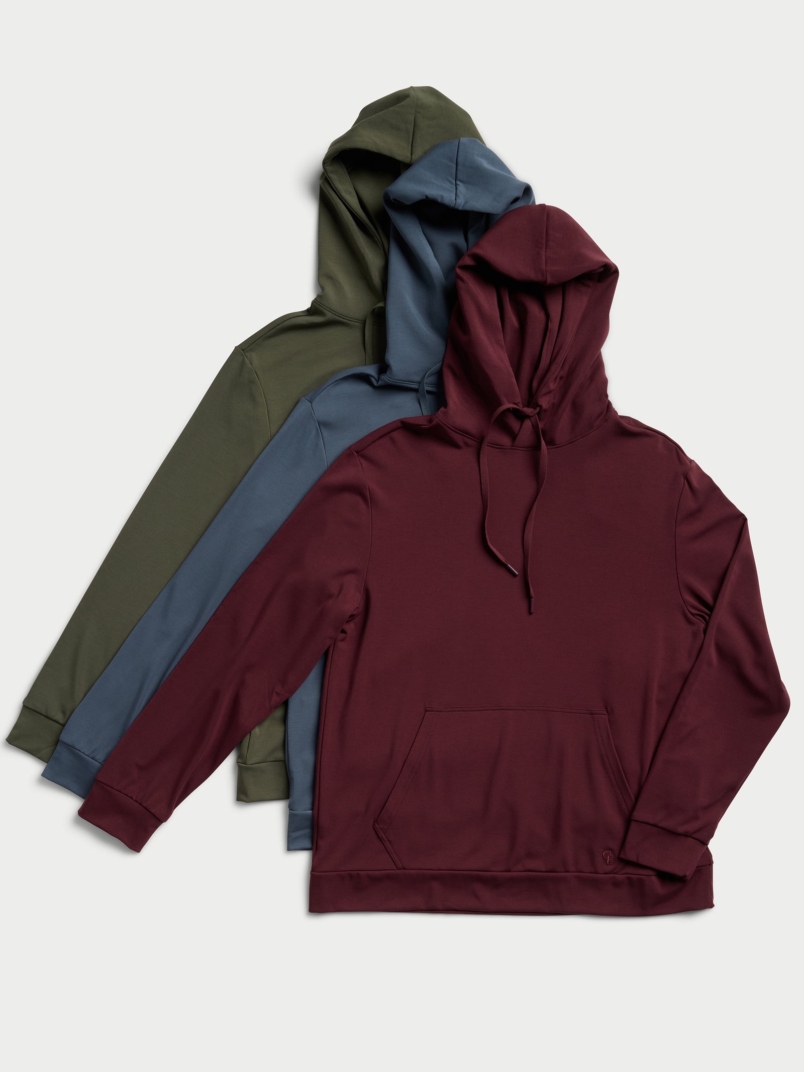 Three Men's Ultra-Soft Bamboo Hoodies from Cozy Earth, featured in olive green, slate blue, and burgundy, are neatly stacked on a light background. Each pullover is designed with a front pocket and drawstring hood. 