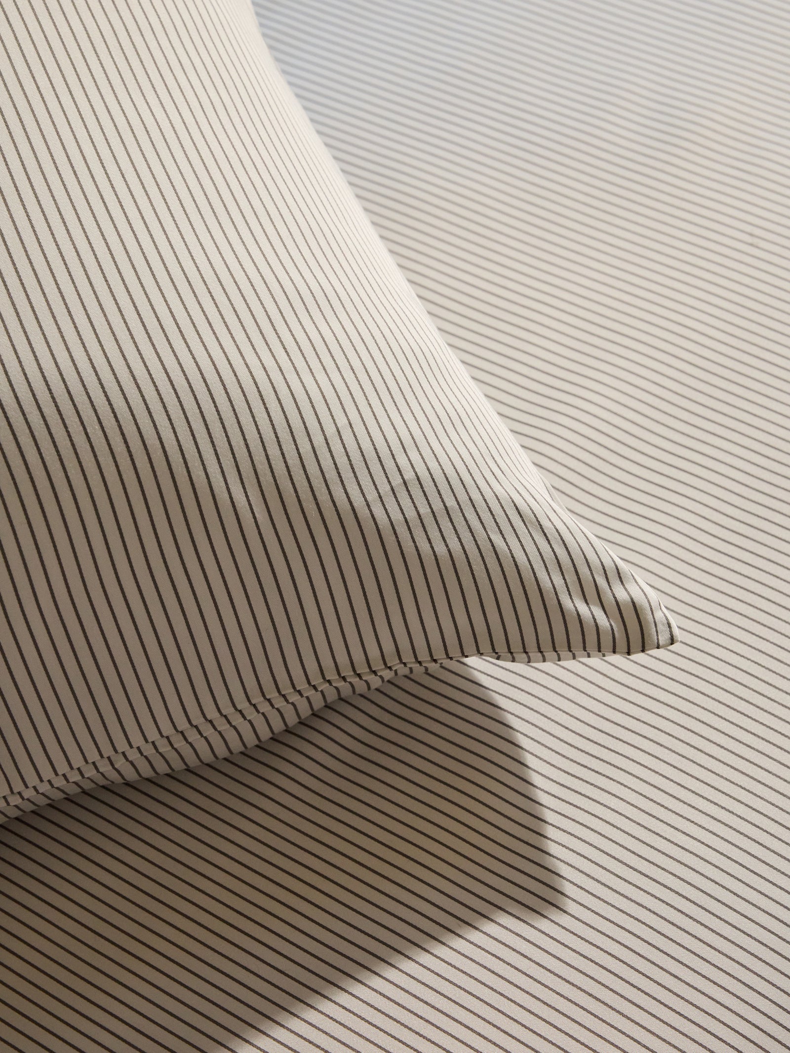 A close-up showcases the Bamboo Pillowcases by Cozy Earth, neatly placed with their thin, dark vertical stripes harmonizing with a matching striped bedsheet. Soft lighting casts gentle shadows, accentuating the texture and pattern of the fabric. 