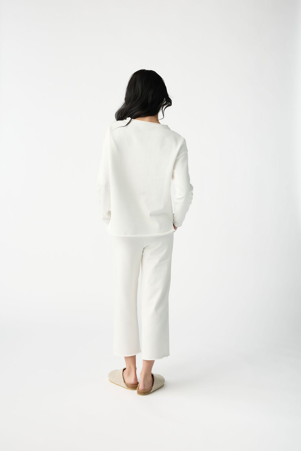 A woman with dark hair wears Cozy Earth Women's Chelsea Cropped Pant in Bone in front of a white background. She is facing away from the camera. |Color:Bone