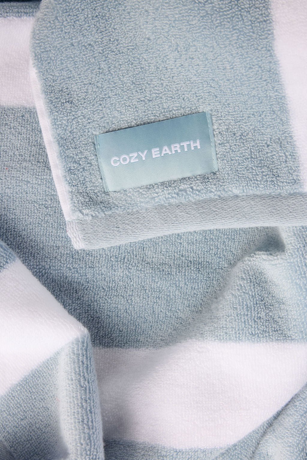 The Classic Stripe Resort Towel from Cozy Earth is pictured, featuring a plush, comfortable texture with soft blue and white stripes. 