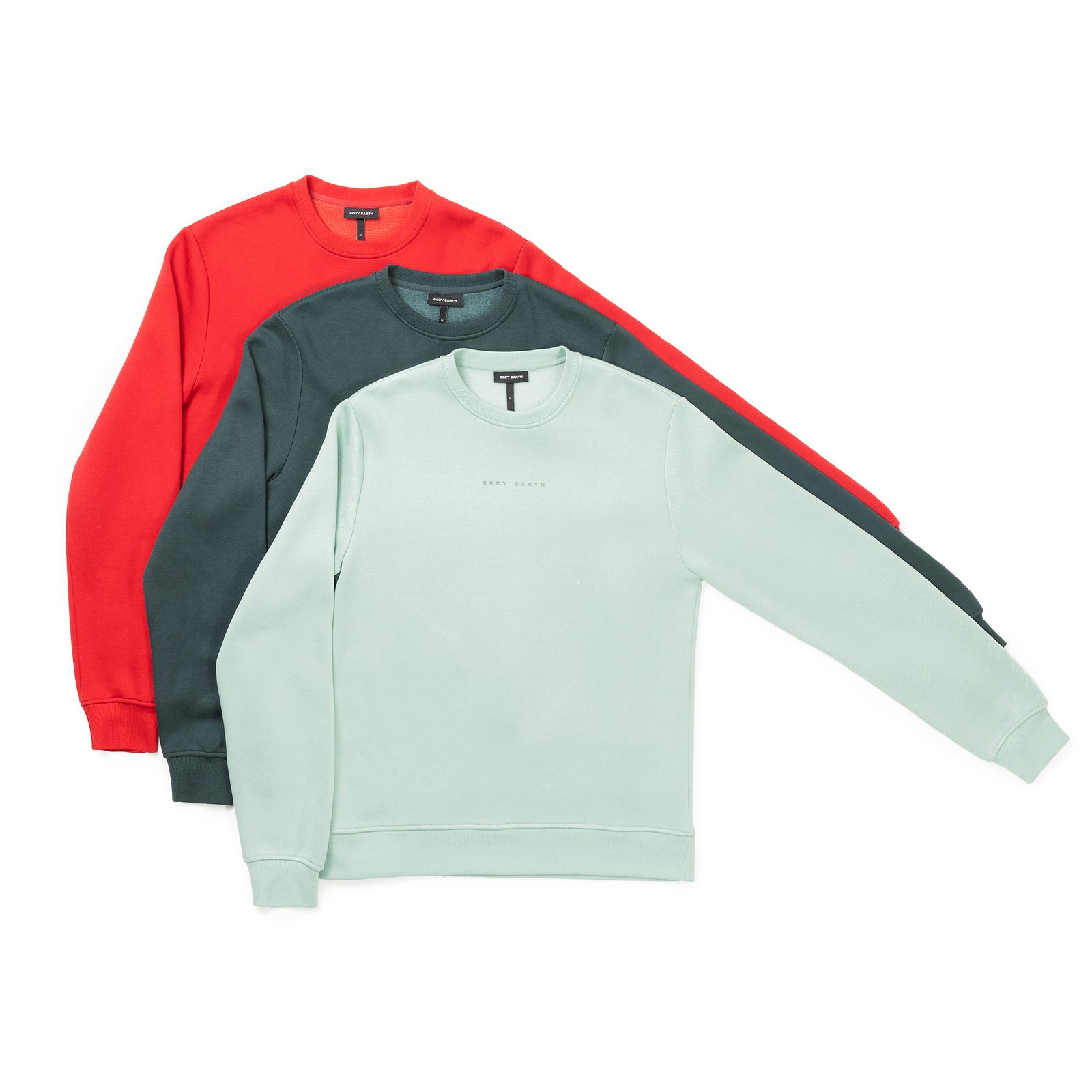 Three Men's CityScape Crewneck sweatshirts from Cozy Earth are arranged overlapping each other in red, dark green, and light mint green from back to front. The fabric looks soft, and the design is minimalist with no visible logos or patterns. 