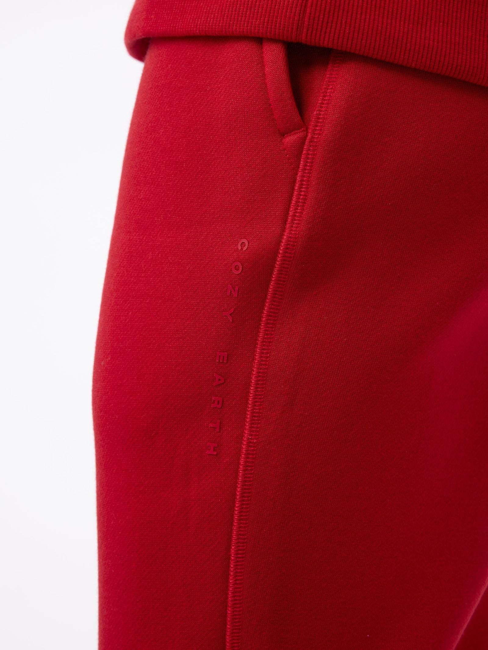 Close-up of the Men's CityScape Jogger in red, featuring a side pocket with "Cozy Earth" embroidered vertically. The texture appears soft and smooth, highlighting the comfortable fabric. The focus is on the stitching and fabric detail. 