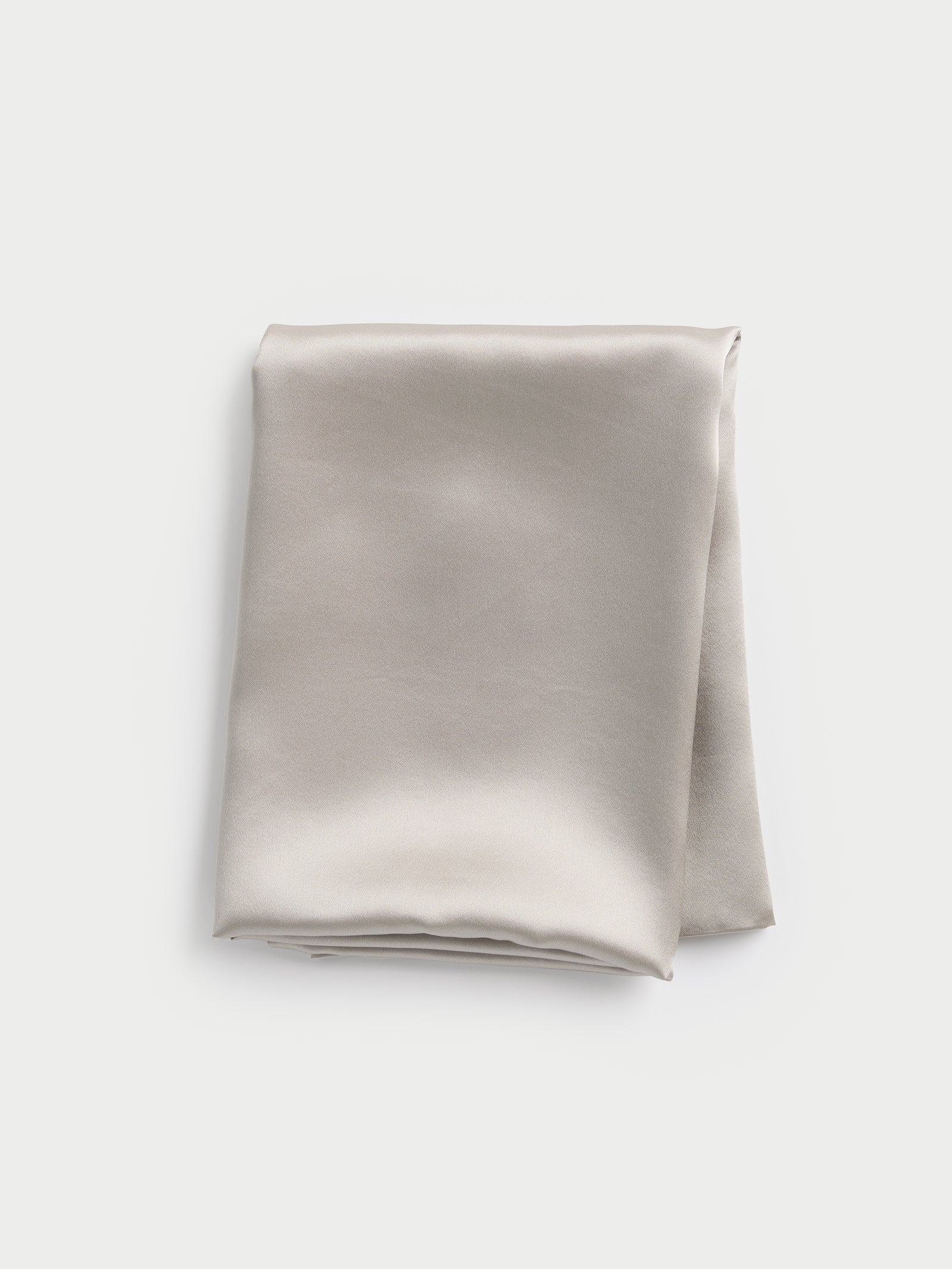 A neatly folded Silk Pillowcase by Cozy Earth in light gray satin rests on a plain white background, showcasing its smooth texture and subtle sheen for a luxurious appearance. 