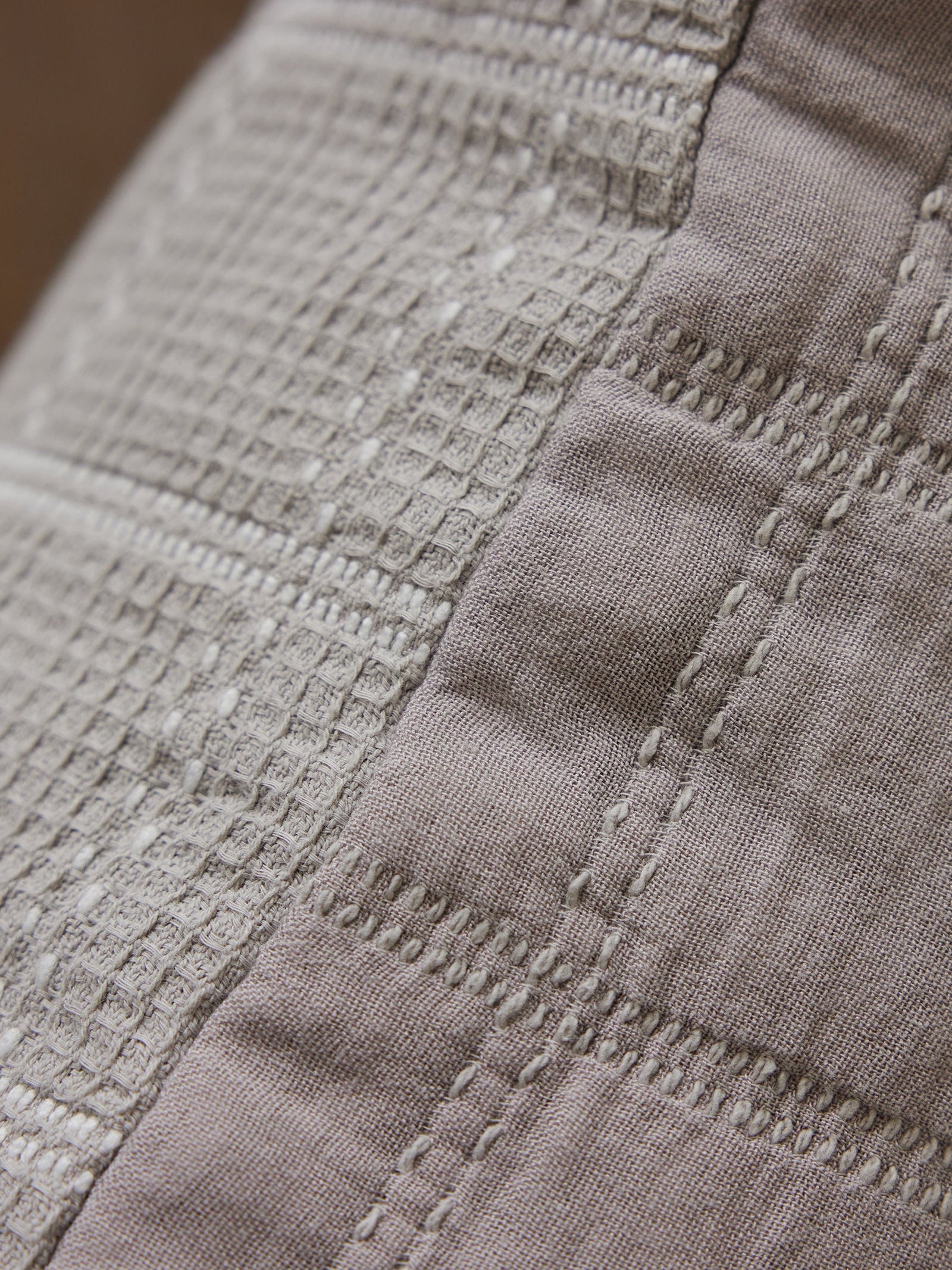 Close-up image of the Waffle Windowpane Pillow by Cozy Earth. The pillow's textured fabric features intricate stitching patterns with a blend of grid-like and linear designs in neutral tones, creating a detailed and tactile appearance. 