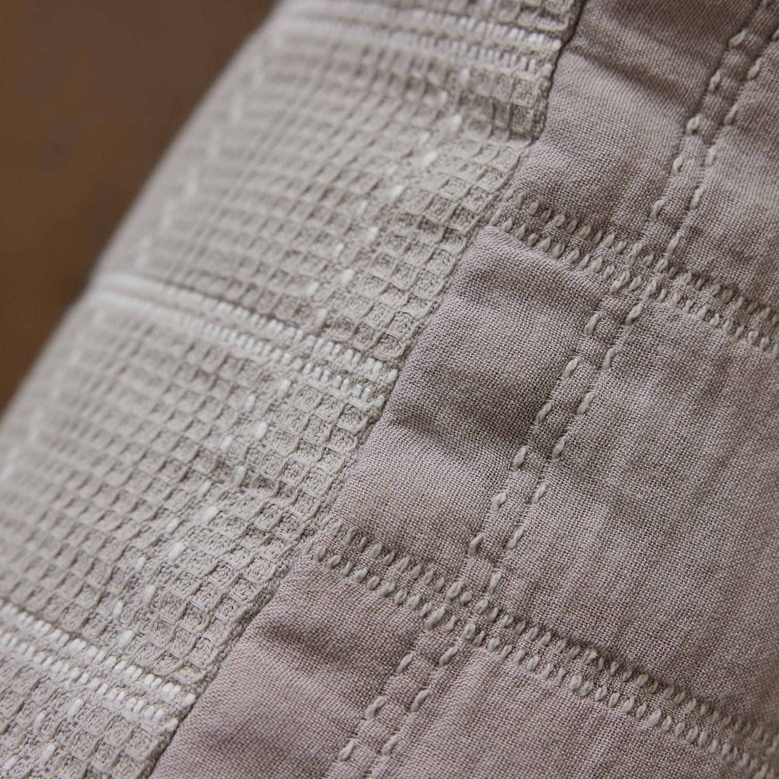 A close-up shot of the Waffle Windowpane Pillow by Cozy Earth, showcasing its textured fabric with a grid-like pattern and visible stitching. The light brown color highlights the intricate details of the weave and seams, indicative of its high-quality craftsmanship. 