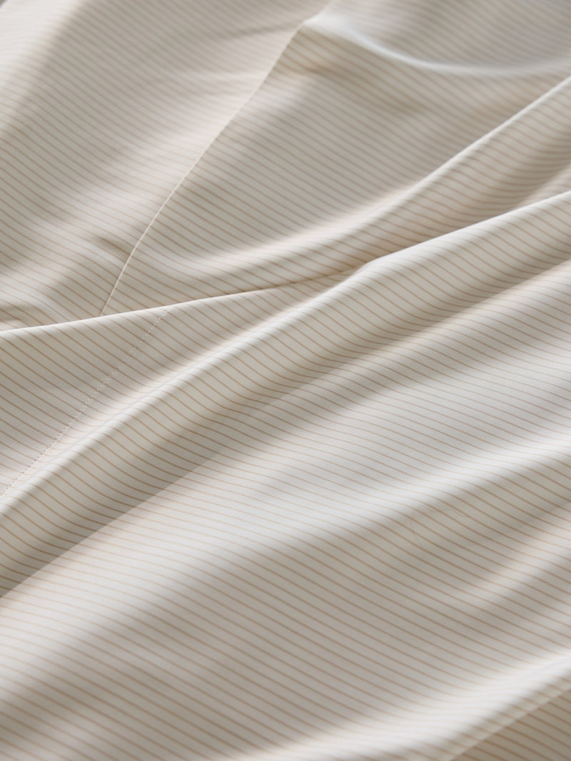 Close-up of the Bamboo Duvet Cover by Cozy Earth, showcasing its smooth, white fabric adorned with thin, light beige stripes running diagonally. The duvet cover is gently folded, creating soft waves and subtle shadows.